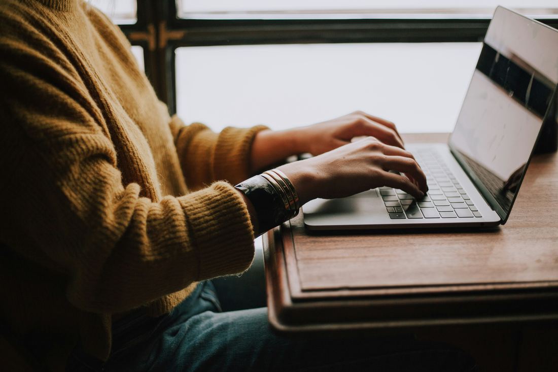 Osoba pisze na klawiaturze laptopa, siedząc przy oknie